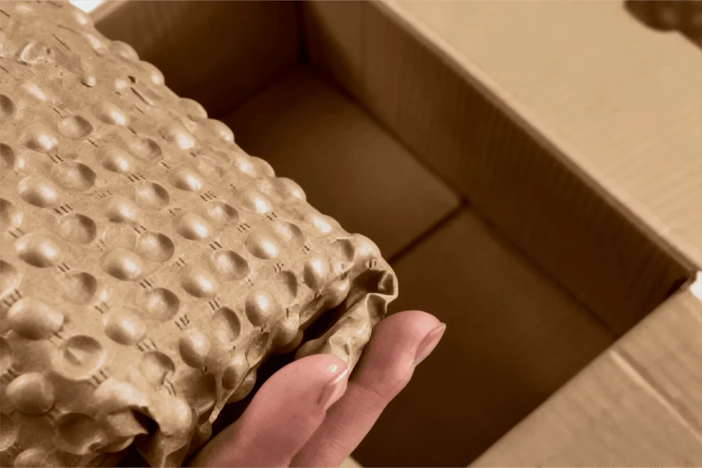 Hands placing paper bubble wrap into a shipping box for protective packaging