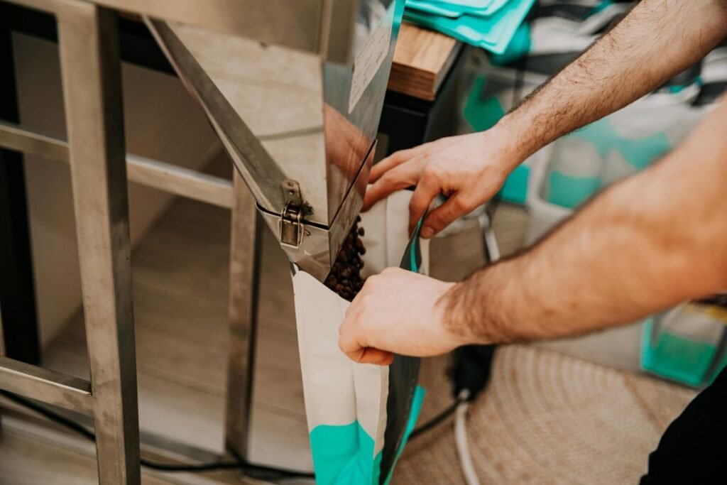 Hands filling pre-opened bags on an automated bagging machine at a warehouse/packing station, illustrating efficient small-item packaging workflow.