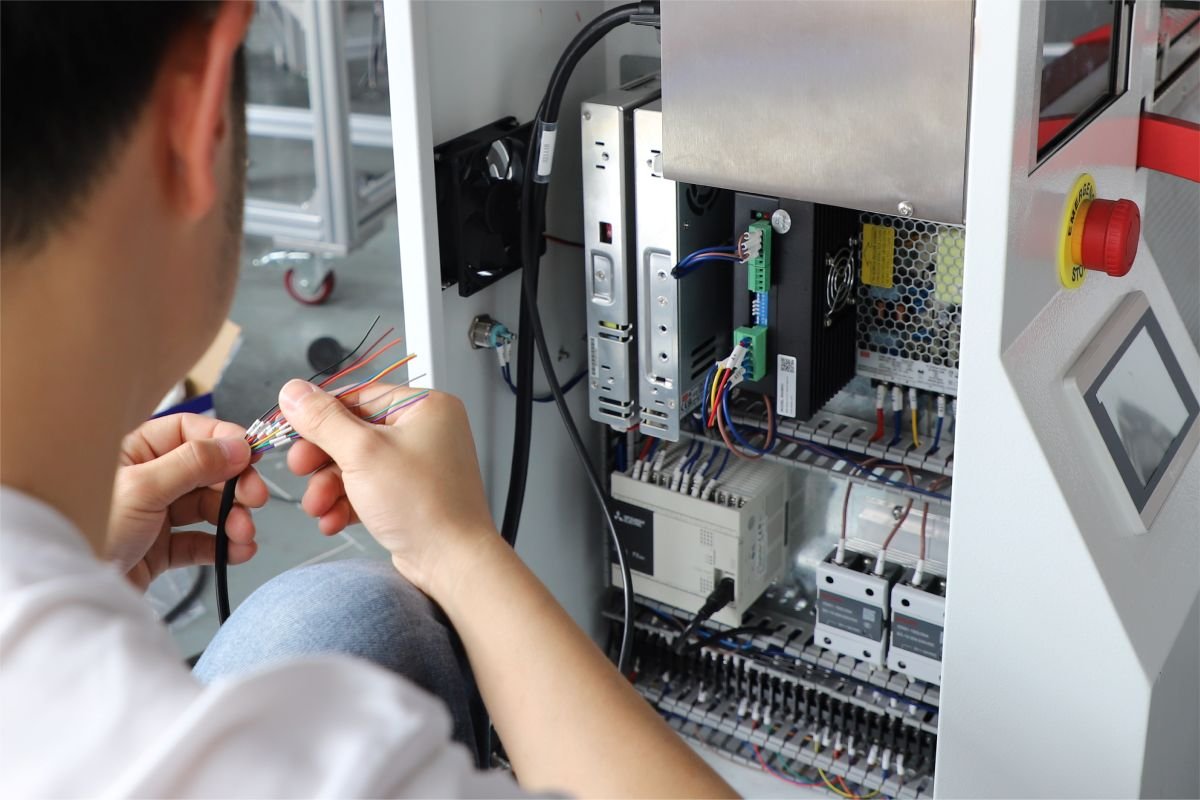 Technician connecting control wires inside an automatic bagging machine panel