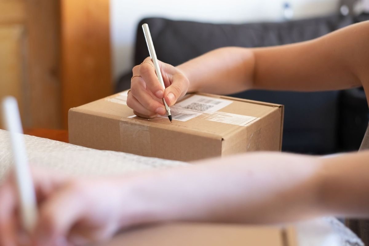 Person writing on a sealed shipping carton during final packing and labeling checks
