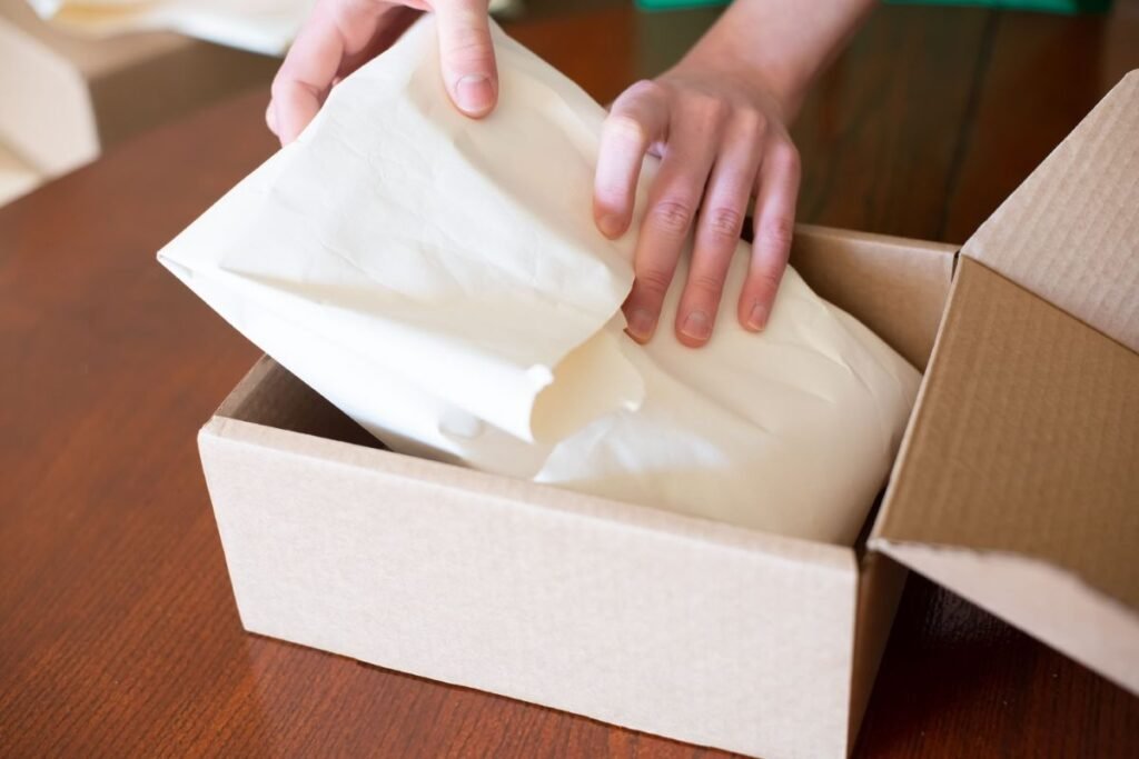 Mãos colocando material de embalagem protetora em uma caixa de papelão para um fluxo de trabalho de embalagem repetível.