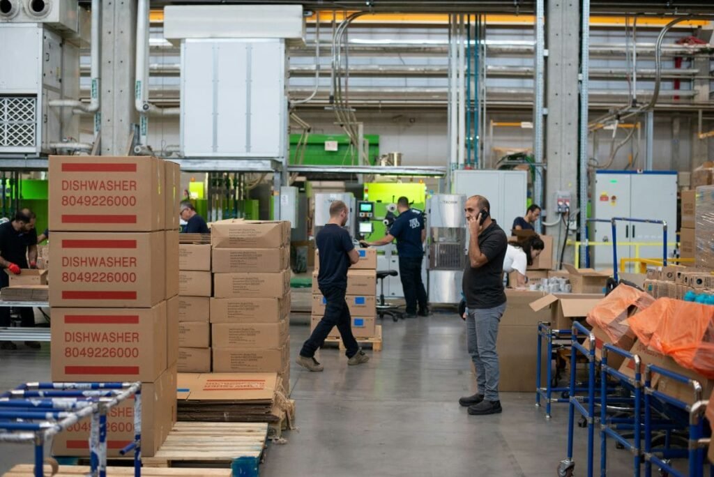 Produktionshalle für Haushaltsgeräte mit Kartons, die für die schützende Schaumverpackung vorbereitet sind.