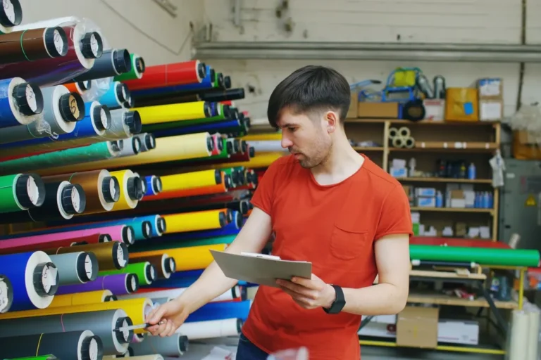 Un ouvrier inspecte les rouleaux de film d'emballage pour vérifier leur compatibilité avec la machine à film rétractable.
