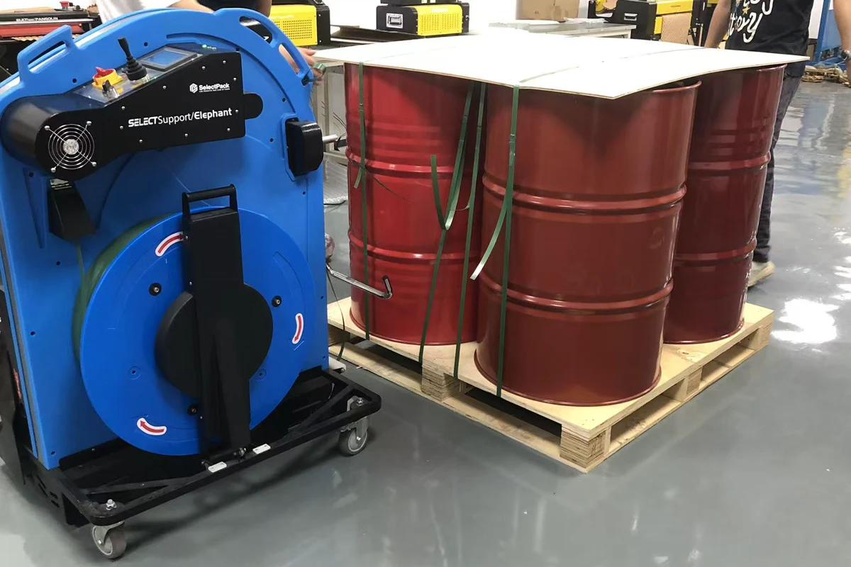SelectPack Elephant beside four red steel drums on a wooden pallet with a top board and green straps.