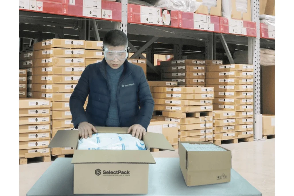 Operator placing a foam packaging bag inside a cardboard box at a packing table.